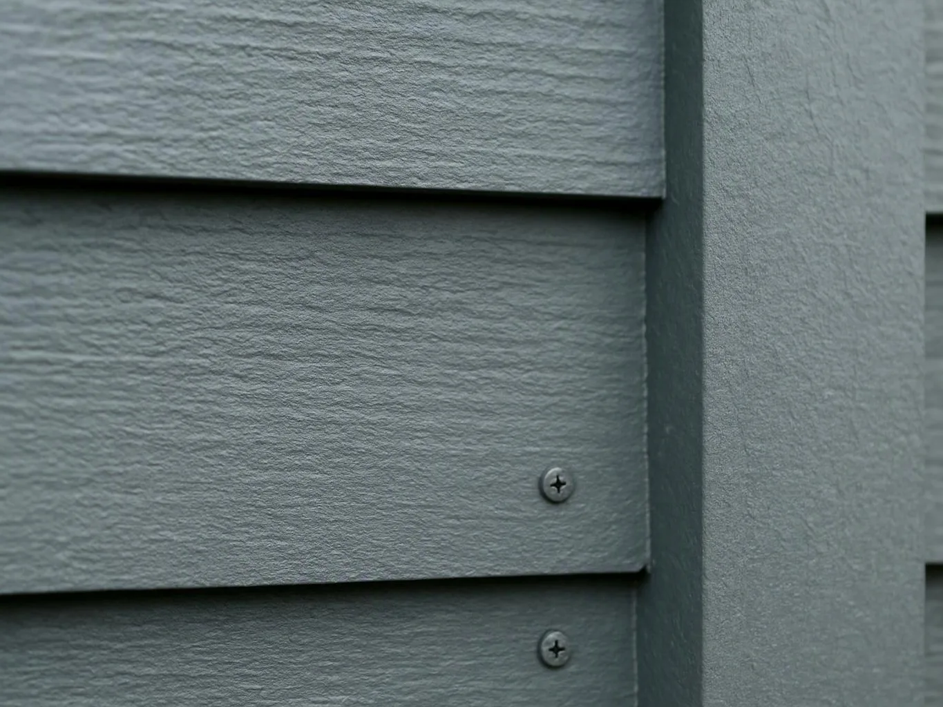 Close-up of gray textured siding boards fastened with small screws on a wall corner