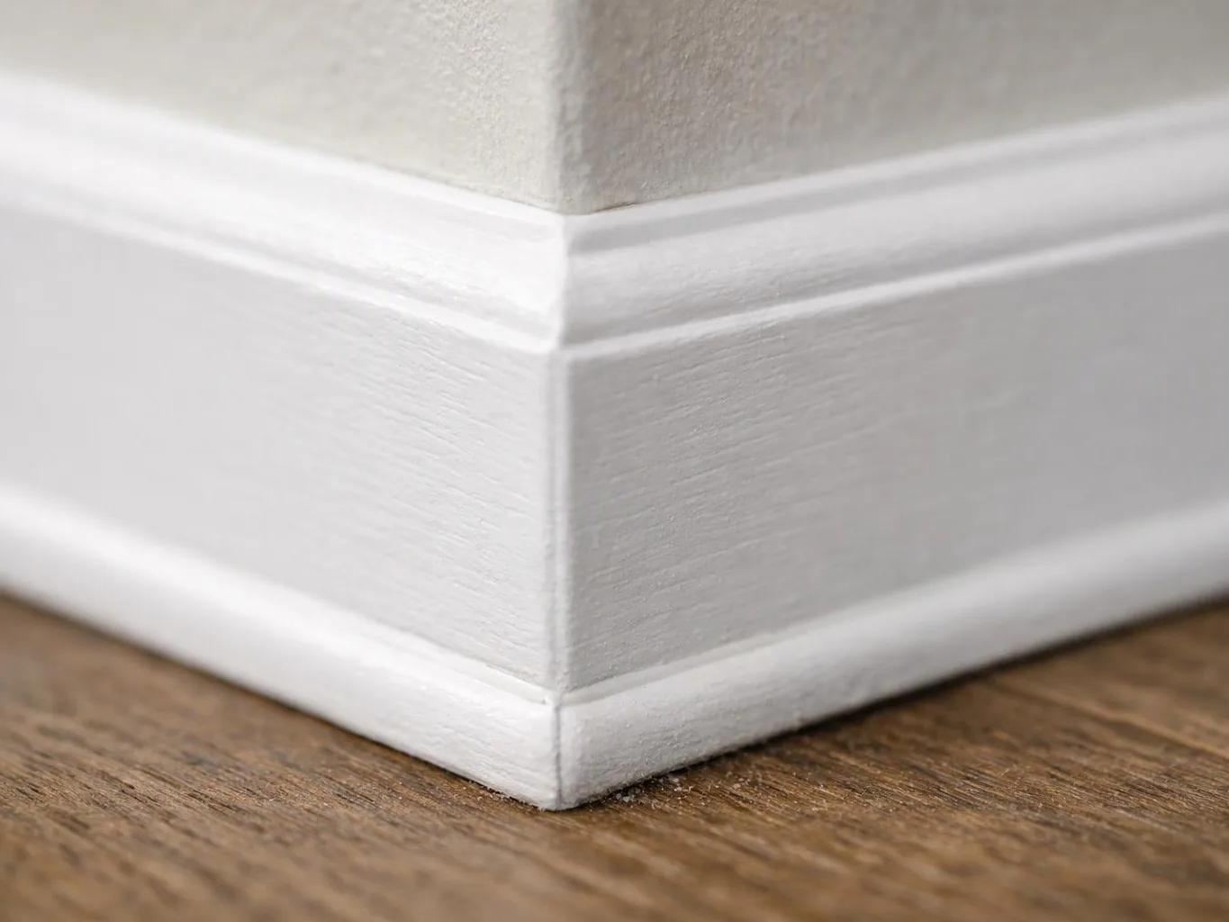 Close-up of a white painted baseboard corner meeting a textured wall above a wood floor
