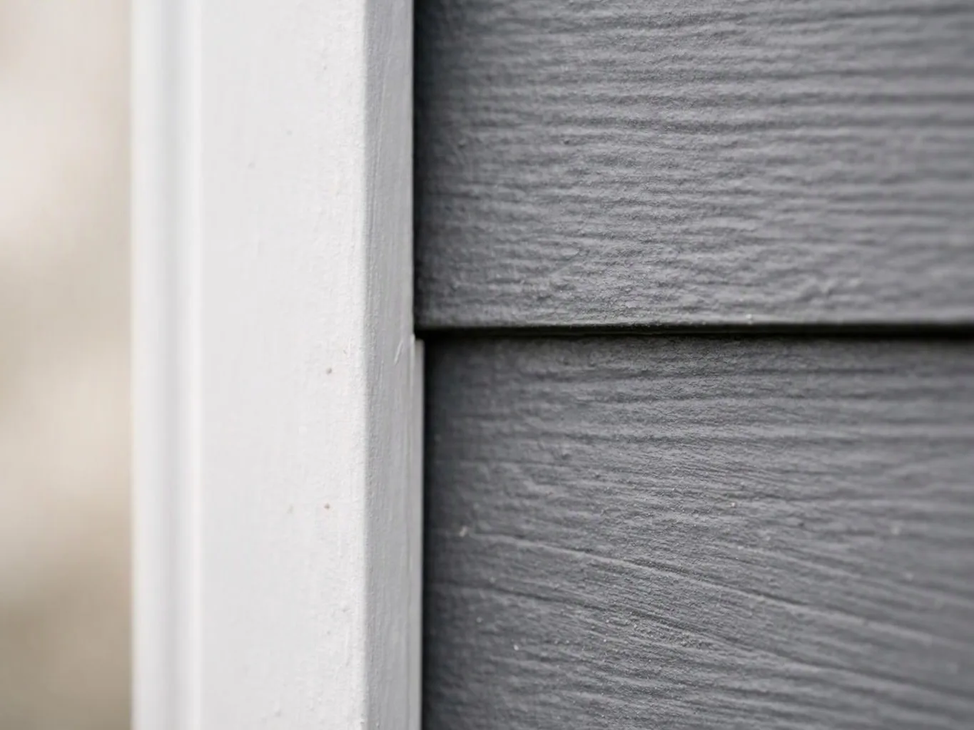 Close-up of white trim beside gray textured siding on a house exterior