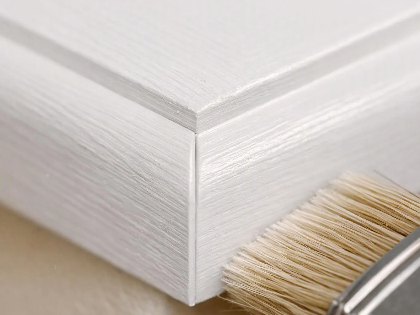 A paintbrush coats the corner of a white wooden box with fresh paint