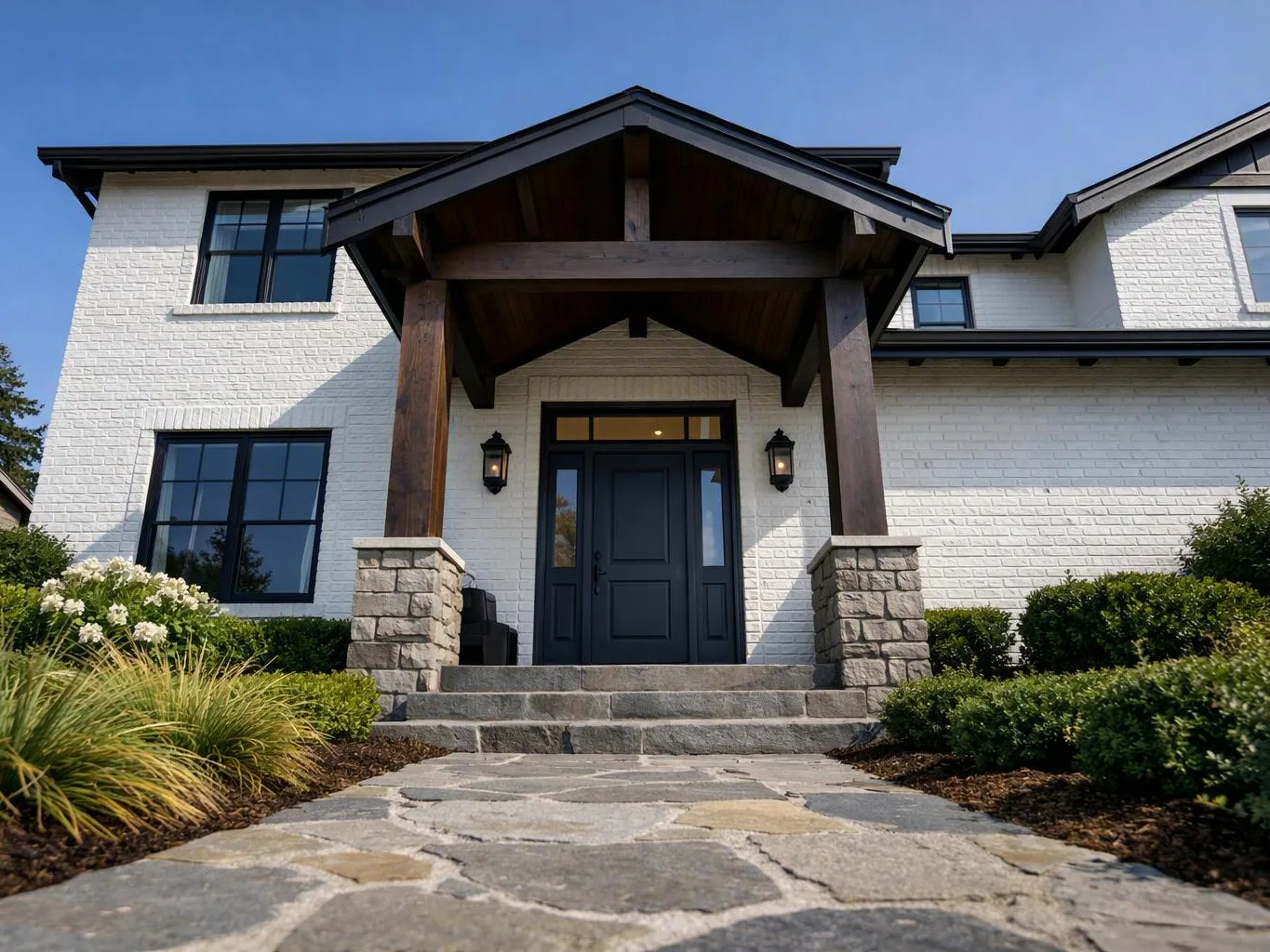 A white brick house with a dark front door, stone steps, and a wood porch roof sits under a blue sky